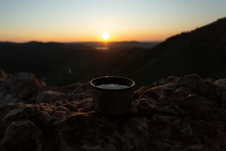 Caneca escura sobre pedras com montanhas iluminadas ao amanhecer